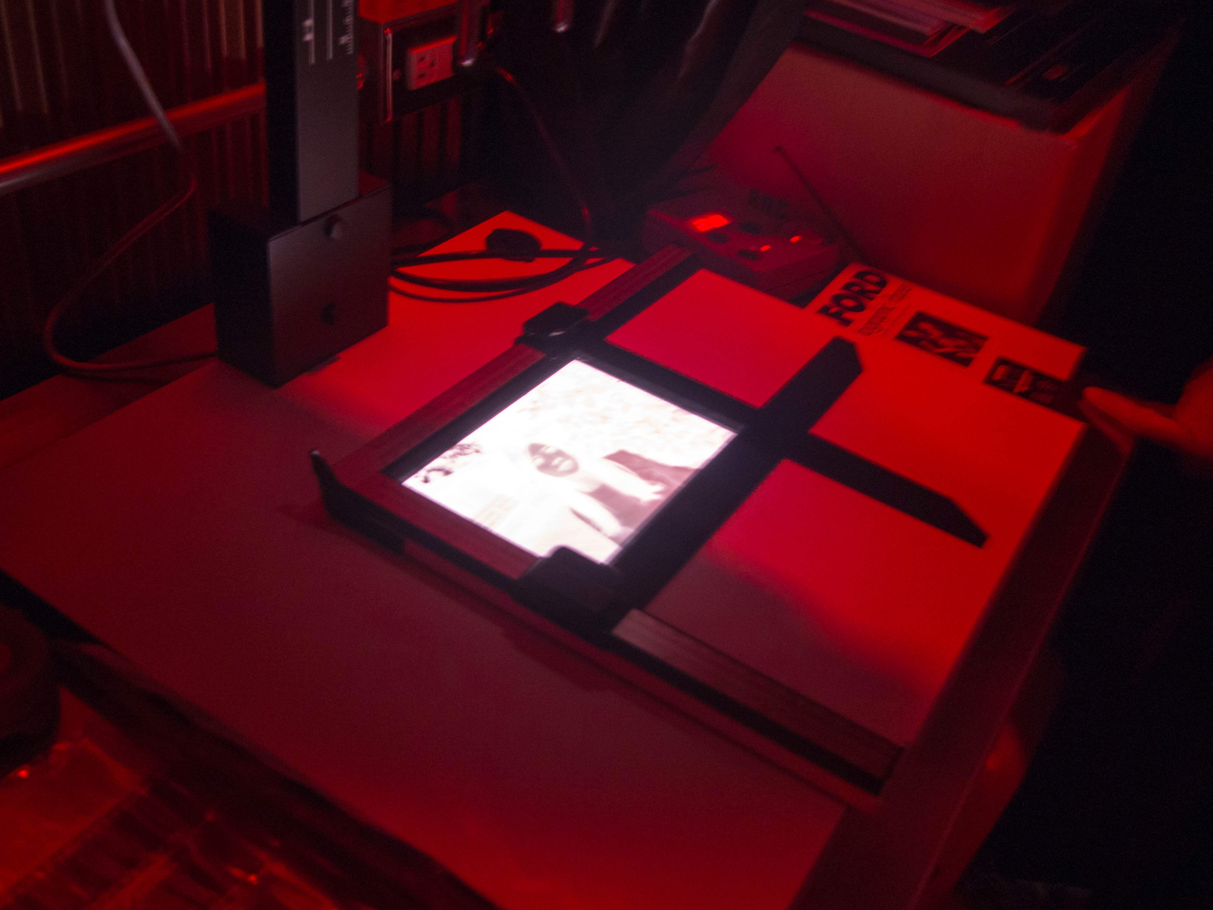 暗房內部使用的是不影響相片曝光的紅光，這台是讓底片放大到相紙的放大機。